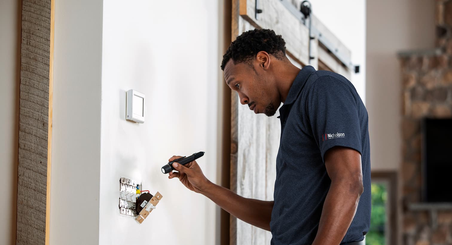 A professional Nicholson electrician using a flashlight to safely inspect and troubleshoot exposed residential wall switch wiring during an electrical repair service.